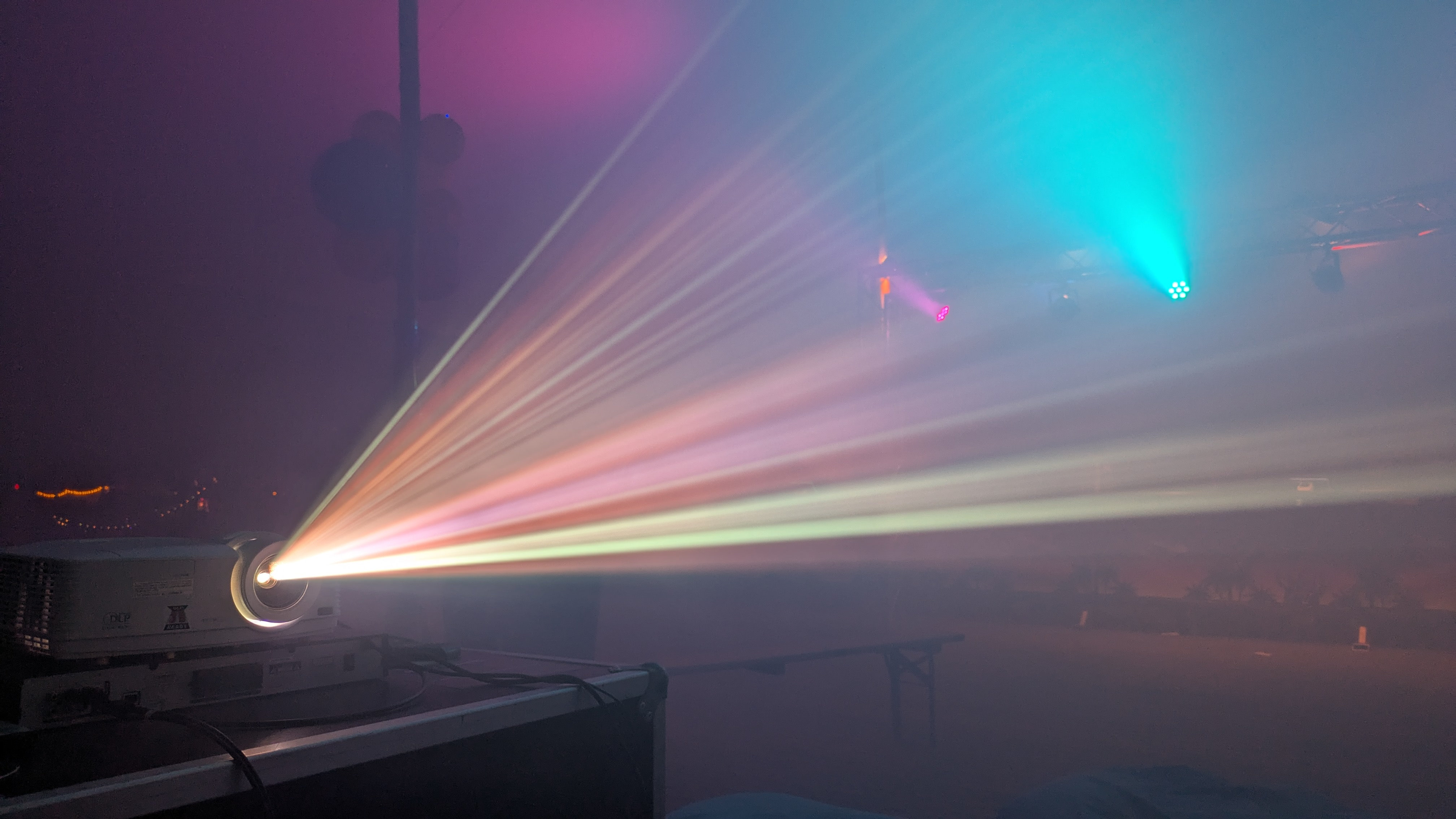 A projector running at the party bar, producing rays of colorful lights in the fog
